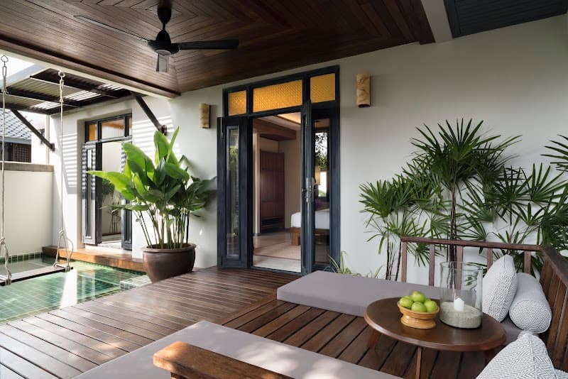 A serene tropical resort patio features lush greenery, wooden flooring, and cozy seating, creating an inviting atmosphere ideal for relaxation and leisure travel in Thailand.