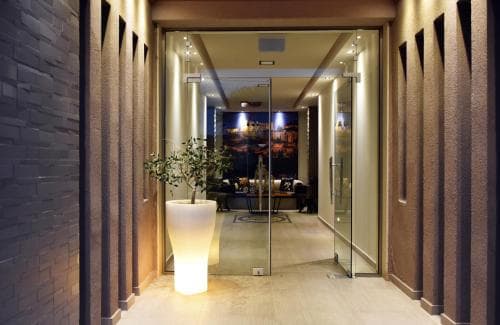 A warmly lit hotel lobby features modern decor with a sleek glass door entrance, a glowing white planter, and inviting seating area, perfect for travelers seeking a cozy yet stylish accommodation.