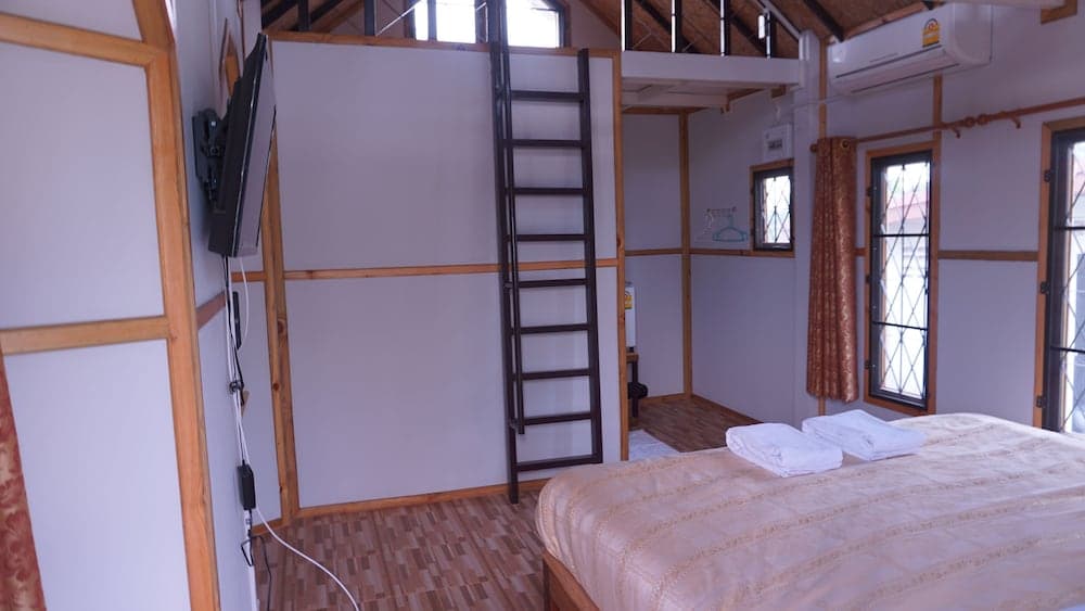 A cozy loft-style bedroom with wooden accents, a ladder leading to an upper level, and neatly arranged towels on the bed invites travelers seeking a comfortable and unique accommodation experience.