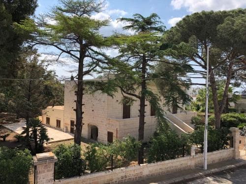 A serene stone villa surrounded by lush green trees under a bright blue sky offers a tranquil retreat, ideal for travelers seeking a peaceful countryside escape.