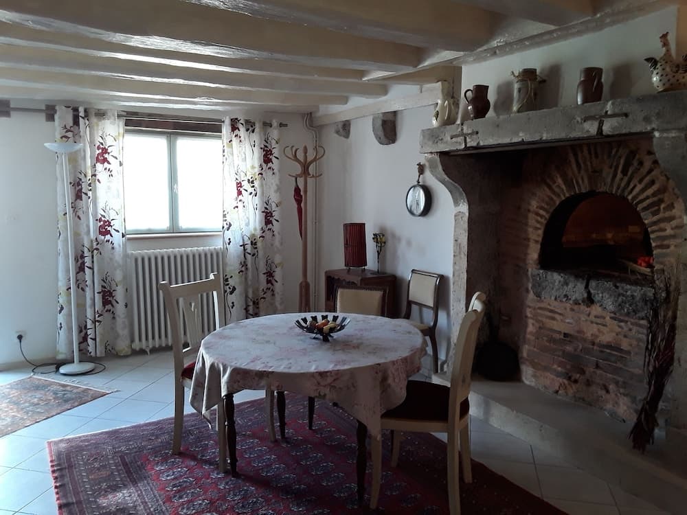 A cozy dining area with a round table on a patterned rug, set against a rustic brick fireplace adorned with decorative vases, evokes a warm, inviting atmosphere perfect for a countryside retreat.