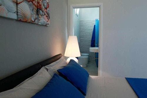 A cozy bedroom with a neatly made bed, blue accents, and a modern lamp creates a serene atmosphere, ideal for travelers seeking a comfortable stay in a compact apartment near amenities.