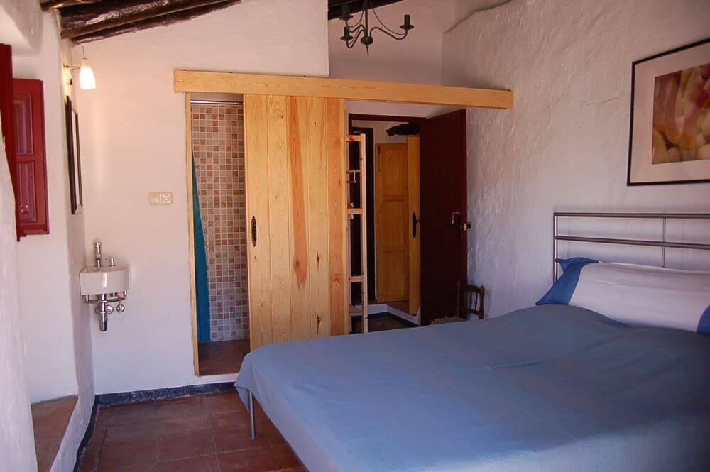 A cozy bedroom with rustic wooden doors, tiled floors, and a blue bedspread invites travelers seeking a serene and charming accommodation experience.