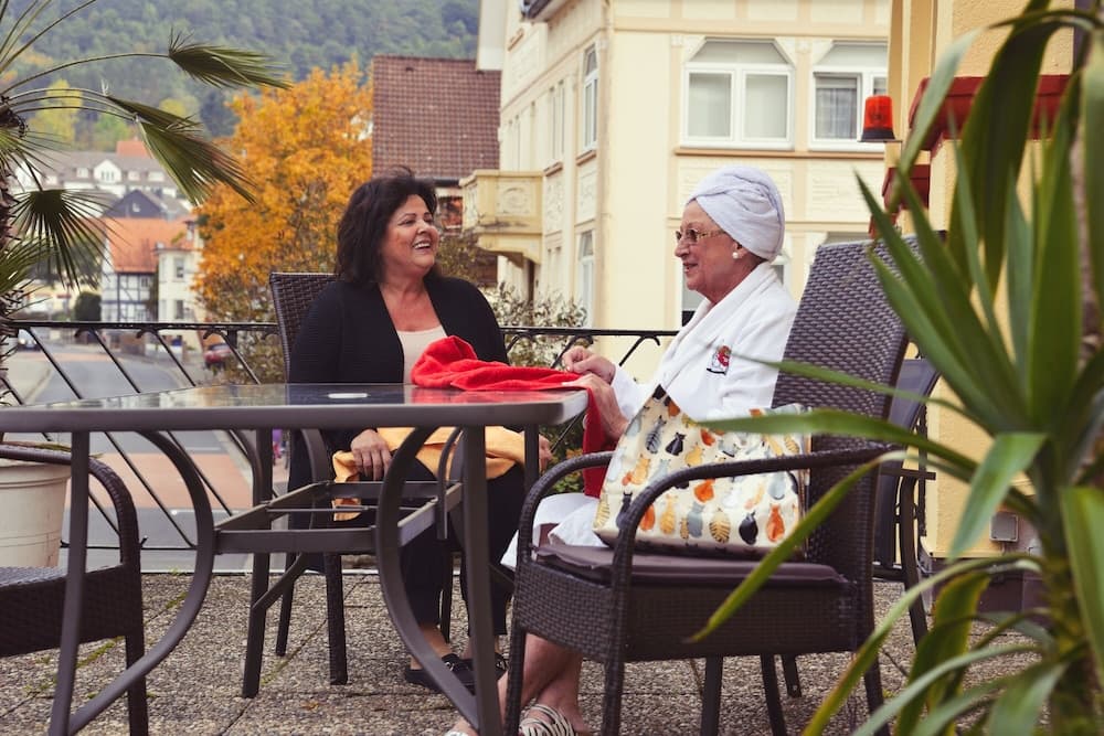 Two women share a cheerful moment on a cozy outdoor patio, surrounded by autumn foliage and quaint town buildings, ideal for a relaxing getaway or family visit.