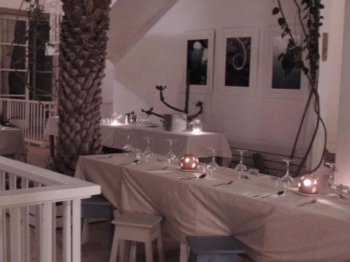 An intimate indoor dining area with white tables set for a romantic evening, featuring candlelight, elegant glassware, and artistic decor, perfect for a cozy dinner date or small celebration.