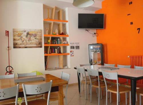 A cozy café with vibrant orange walls, wooden tables, white chairs, and a world map decorates the space, creating an inviting atmosphere perfect for travelers seeking a casual dining spot.