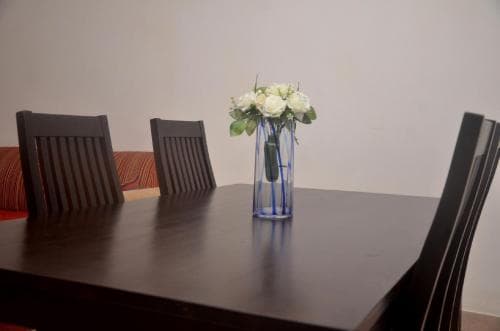 A cozy dining room scene features a polished wooden table adorned with a vibrant blue vase holding fresh white flowers, surrounded by sleek chairs, ideal for travelers seeking comfortable accommodations.