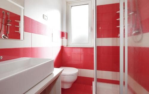 A vibrant red and white tiled bathroom with modern fixtures, including a sink, toilet, and shower, offers a clean and stylish space ideal for travelers seeking a refreshing stay.