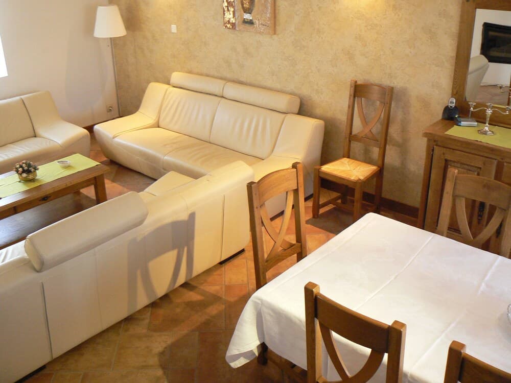 A cozy living room with cream leather sofas, wooden dining furniture, and warm terracotta flooring creates an inviting atmosphere ideal for a relaxing vacation rental.