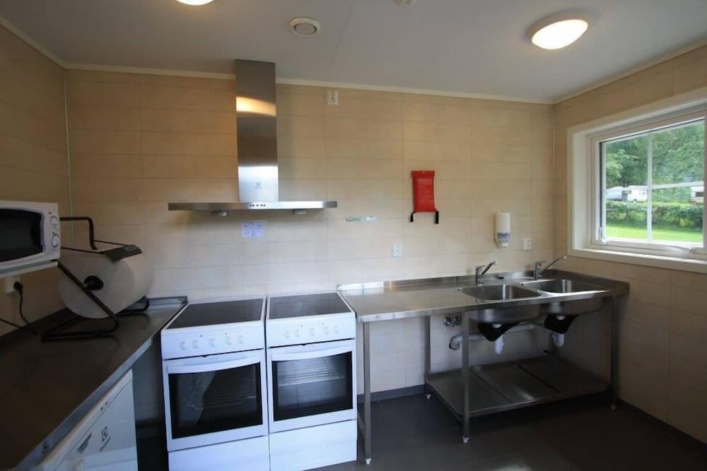 A clean, functional communal kitchen with stainless steel appliances, a double sink, and a view of greenery through the window, ideal for group accommodations or camping facilities.