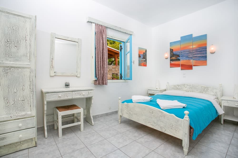 A cozy, sunlit bedroom with rustic white furniture, vibrant blue bedding, and colorful ocean artwork creates a serene retreat ideal for vacation rentals.