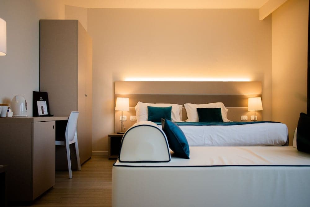 A cozy hotel room features a neatly made bed with teal accents, warm ambient lighting, and a modern desk setup, ideal for travelers seeking comfort and functionality.