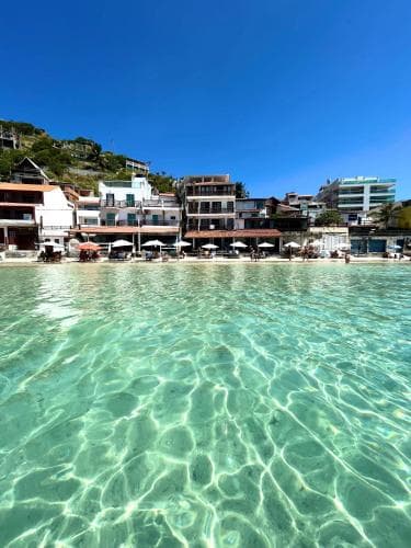 A serene coastal scene features crystal-clear turquoise waters gently lapping against a sandy beach lined with colorful umbrellas and buildings, ideal for a relaxing seaside getaway.