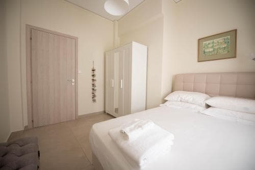 A cozy hotel room features a neatly made bed with white linens, a soft pink headboard, and minimalistic decor, creating a serene atmosphere ideal for travelers seeking relaxation.