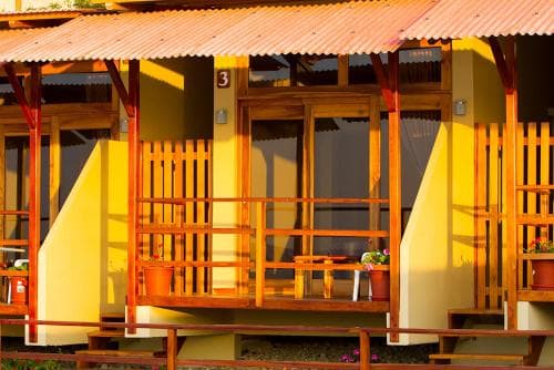 A serene tropical lodge features vibrant yellow walls, wooden balconies adorned with potted plants, and a warm sunset glow, ideal for travelers seeking a peaceful retreat.