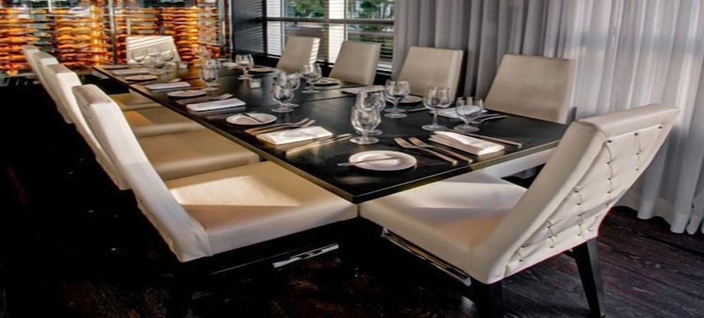 A sophisticated private dining room features a sleek black table set with elegant white chairs, glassware, and fine dining essentials, creating an intimate and luxurious atmosphere ideal for exclusive gatherings or corporate events.