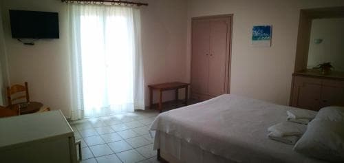 A cozy hotel room with tiled floors, a neatly made bed, wooden furniture, and sheer curtains letting in soft light, ideal for travelers seeking a comfortable and tranquil stay.