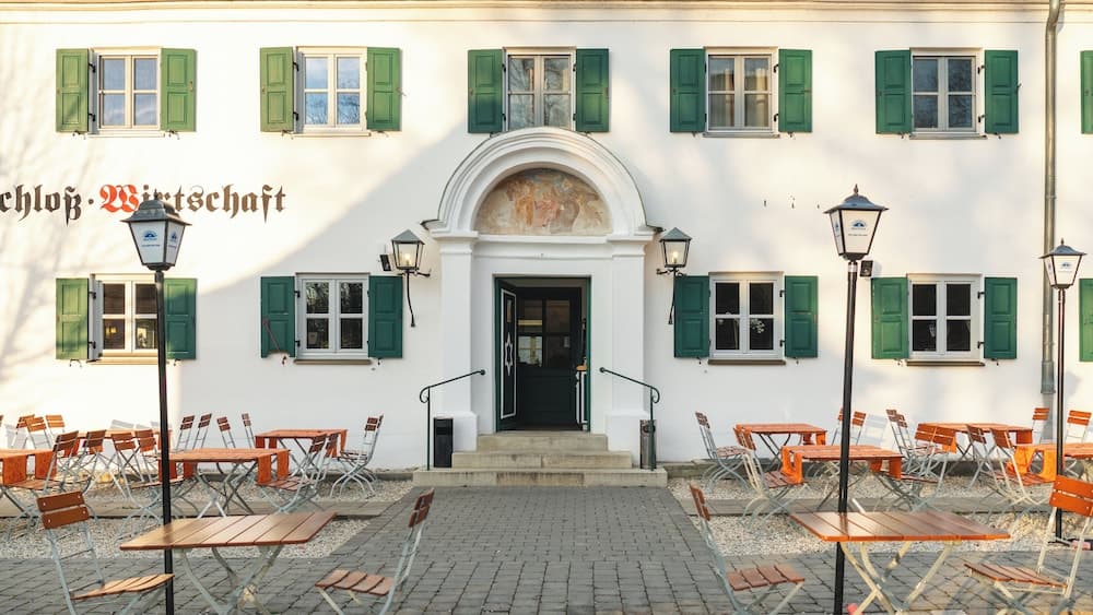 A charming white building with green shutters and an inviting outdoor seating area creates a cozy European café atmosphere perfect for leisurely dining or sightseeing.