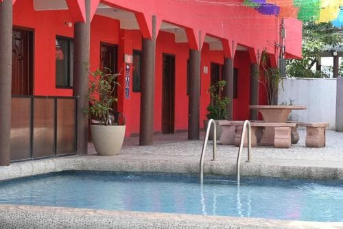 A vibrant red building with a serene poolside area, featuring potted plants and a stone table, creates a relaxing tropical resort atmosphere ideal for vacation stays.