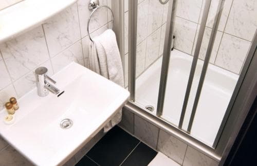 A clean, modern bathroom with white marble tiles, a sleek sink, and a glass-enclosed shower exudes a minimalist vibe, ideal for travelers seeking a refreshing stay in a hotel or guesthouse.