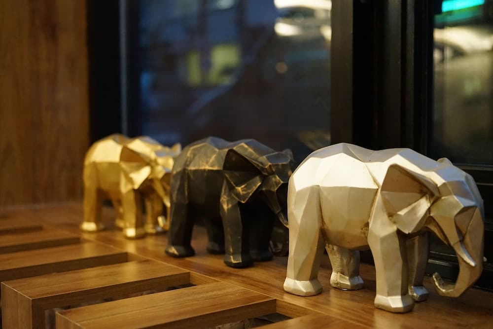 A cozy indoor setting features three geometric elephant sculptures on a wooden surface, creating an artistic and serene atmosphere ideal for travelers seeking unique decor inspiration.