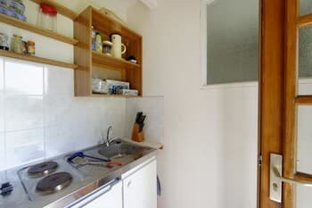 A cozy, compact kitchen with white tiled walls, wooden shelves stocked with essentials, and a stainless steel sink creates a welcoming atmosphere ideal for travelers seeking self-catering accommodations.
