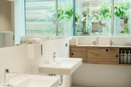 A serene spa bathroom features modern white sinks, wooden accents, and lush greenery visible through large windows, ideal for relaxation and wellness retreats.