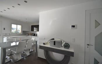 A modern, minimalist apartment interior featuring sleek white furniture, a stylish console table with decorative items, and large windows that invite natural light, ideal for travelers seeking contemporary urban accommodations.