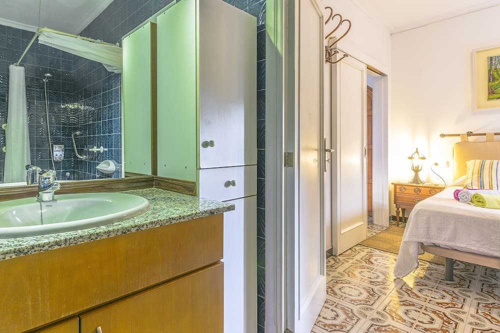 A cozy bedroom with patterned flooring transitions into an adjacent bathroom featuring a green vanity and tiled walls, ideal for travelers seeking comfort and style in their accommodations.