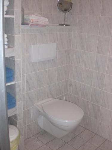 A clean, modern bathroom with marble-look tiles features a wall-mounted toilet, neatly folded towels on shelves, and a small mirror, ideal for travelers seeking comfortable accommodations.