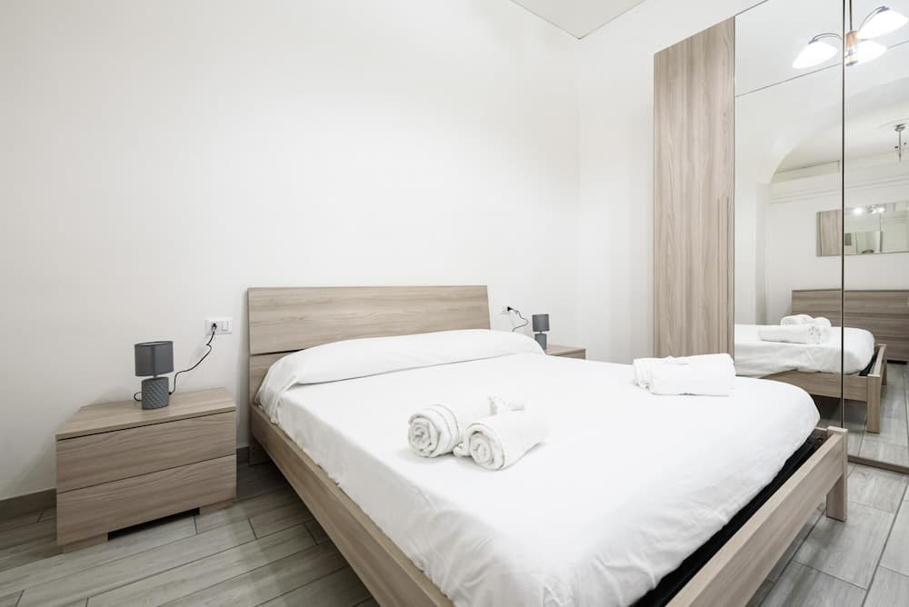 A serene minimalist bedroom with a wooden bed, neatly folded towels, mirrored wardrobe, and soft lighting, ideal for travelers seeking a cozy and modern accommodation experience.