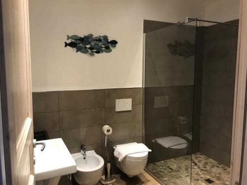 A modern bathroom with sleek tiled walls, a glass-enclosed shower, and fish-themed wall art creates a serene and stylish space ideal for travelers seeking comfort and design in their accommodations.