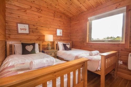 A cozy cabin bedroom with wooden walls, twin beds adorned with heart-patterned pillows, and a bright window view, perfect for a serene getaway retreat.