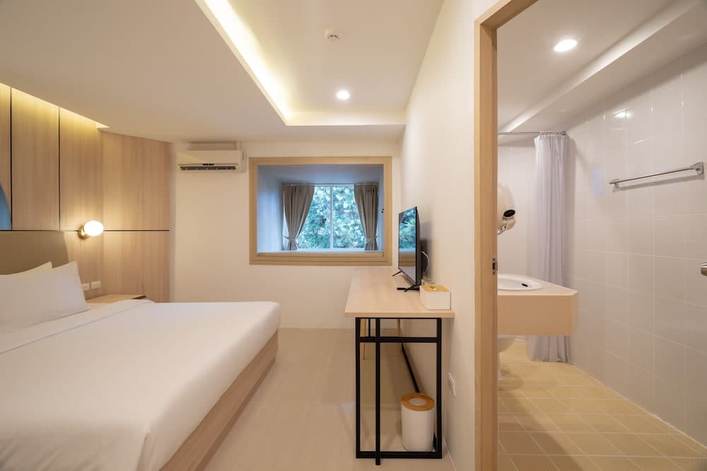 A cozy hotel room with a neatly made bed, wooden furnishings, a desk with a TV, and an adjacent bathroom featuring a shower curtain, ideal for travelers seeking comfort and convenience.