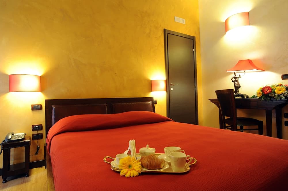 A cozy hotel room with warm yellow walls, a red bedspread, and a breakfast tray featuring croissants and tea cups, ideal for travelers seeking comfort and a welcoming atmosphere.