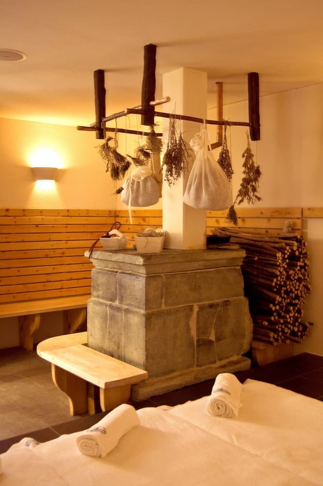 A cozy sauna room with wooden benches, a stone heater, hanging herbs, and neatly rolled towels creates a serene relaxation space ideal for wellness retreats.
