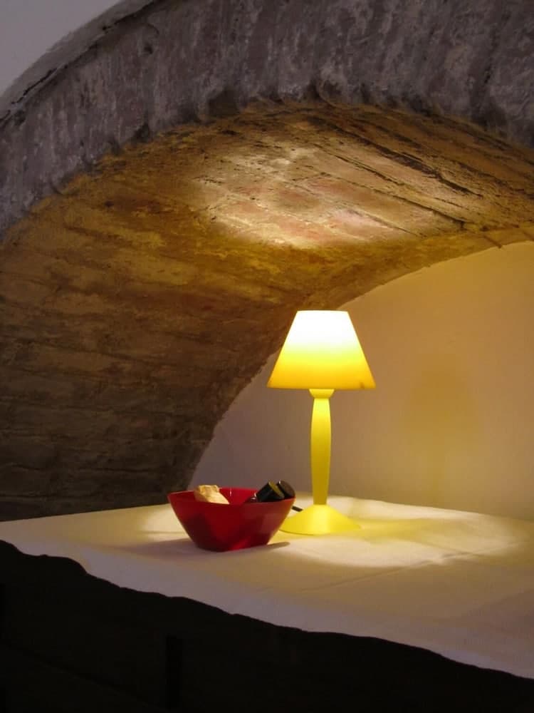 A cozy alcove with a rustic stone archway glows warmly under a yellow lamp beside a red bowl on a white tablecloth, ideal for intimate dining or relaxation in a historic setting.