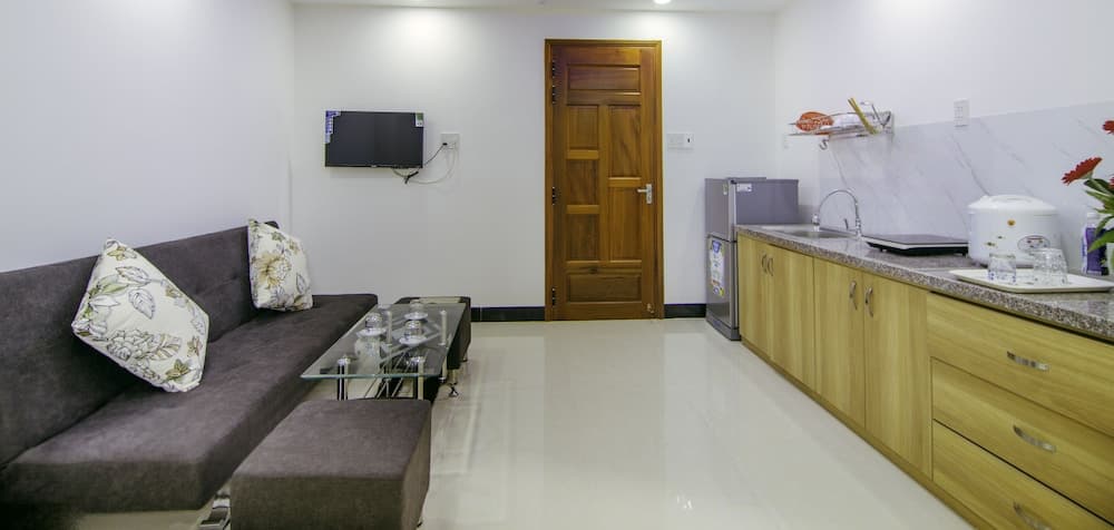 A cozy apartment interior features a modern living space with a plush sofa, glass coffee table, mounted TV, and an adjacent kitchenette with wooden cabinets, ideal for short-term rentals or vacation stays.