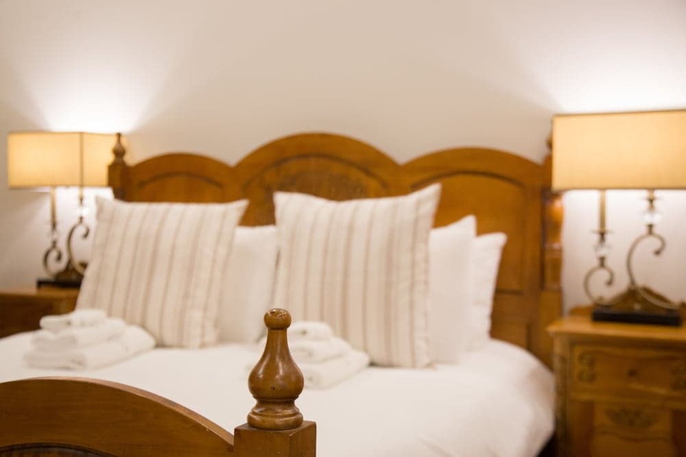 A cozy hotel room features a warmly lit bed with wooden carvings, soft white linens, and matching bedside lamps, ideal for travelers seeking comfort and relaxation.