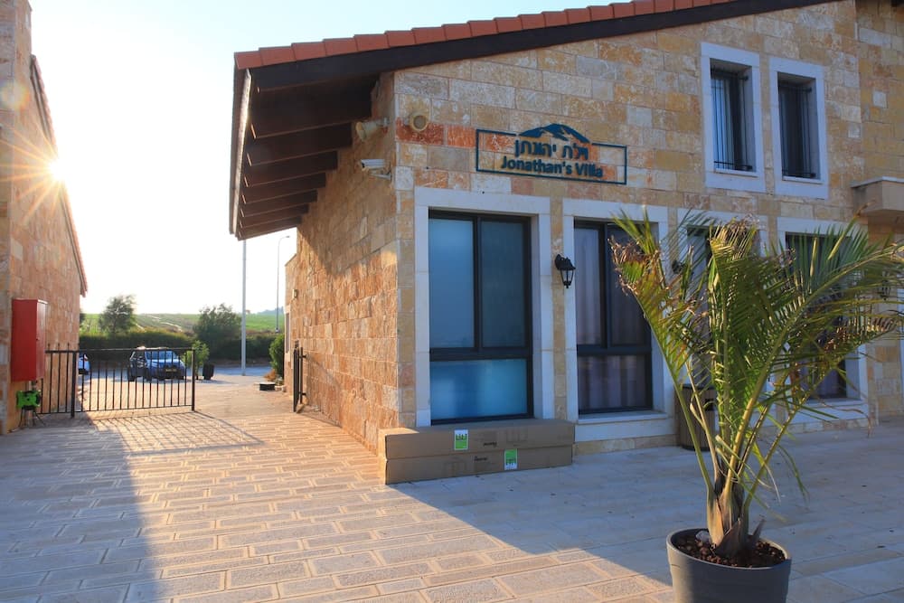 A serene stone villa with a tiled patio, potted palm plant, and "Jonathan's Villa" sign bathed in warm sunlight, ideal for travelers seeking a cozy retreat.