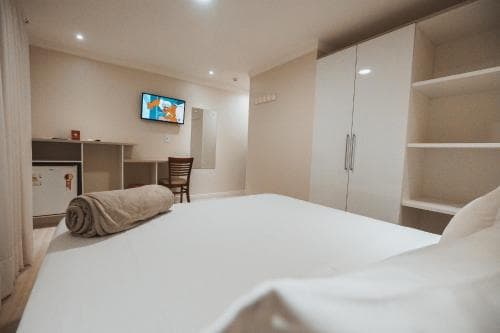 A cozy hotel room features a neatly made bed, a mounted TV, and minimalist furniture, creating a serene atmosphere ideal for travelers seeking comfort and simplicity.