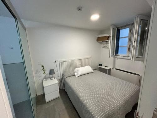 A cozy minimalist bedroom with a neatly made bed, small bedside tables, and an open window letting in natural light, ideal for travelers seeking a simple and serene accommodation experience.