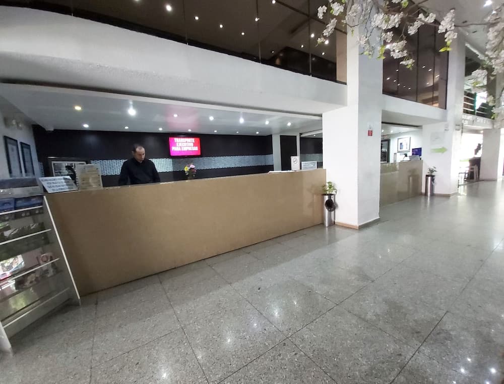 A modern hotel lobby features a reception desk with digital signage, decorative floral elements, and a clean, polished floor, ideal for travelers seeking a professional and welcoming atmosphere.
