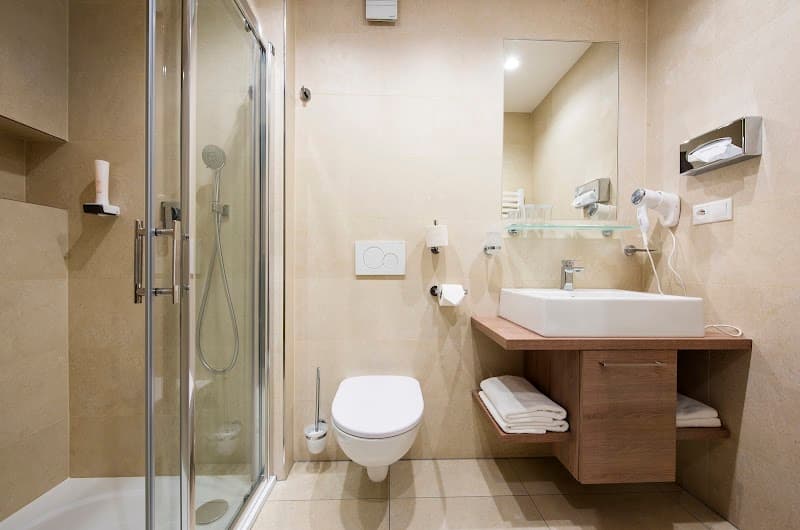 A cozy and modern bathroom at the Hotel Panorama Resort in Štrbské Pleso, Slovakia, features a sleek shower, a wooden vanity with a sink, neatly folded towels, and a hairdryer, ideal for travelers seeking comfort and convenience during their mountain getaway.