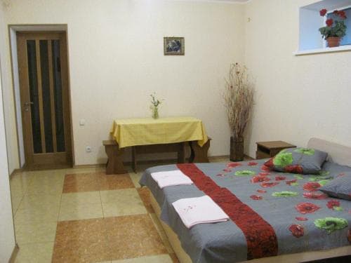 A cozy bedroom with a neatly made bed adorned with floral bedding, a wooden bench draped in yellow cloth, and a small window with potted plants, ideal for travelers seeking a comfortable and inviting accommodation.