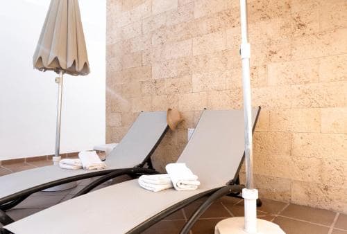 A serene indoor relaxation area features two lounge chairs with neatly folded towels, a closed umbrella, and a tiled wall backdrop, ideal for travelers seeking a tranquil spa retreat experience.