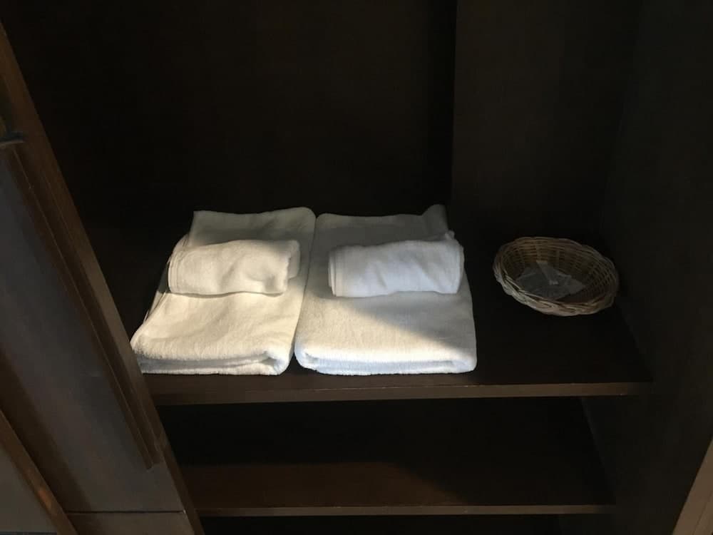 A cozy hotel closet features neatly folded white towels on a dark shelf alongside a small wicker basket, ideal for travelers seeking comfort and organization in their accommodations.