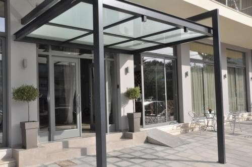 A modern hotel entrance features sleek glass and metal architecture, inviting potted plants, and a spacious patio area, ideal for travelers seeking upscale accommodations with a contemporary aesthetic.