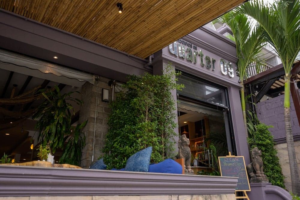 A cozy outdoor seating area with lush greenery, bamboo ceiling, and stone lion statues invites travelers to relax at a charming café, perfect for enjoying local promotions and tropical ambiance.