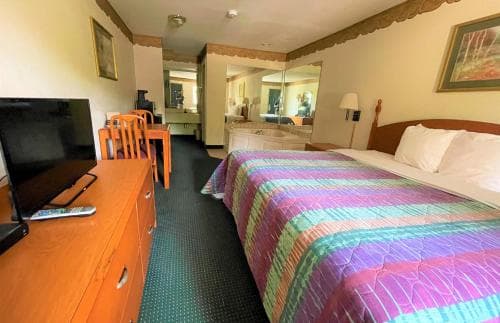 A cozy motel room features a vibrant striped bedspread, wooden furniture, and a mirror-lined vanity area, creating a welcoming atmosphere ideal for travelers seeking comfort and convenience.
